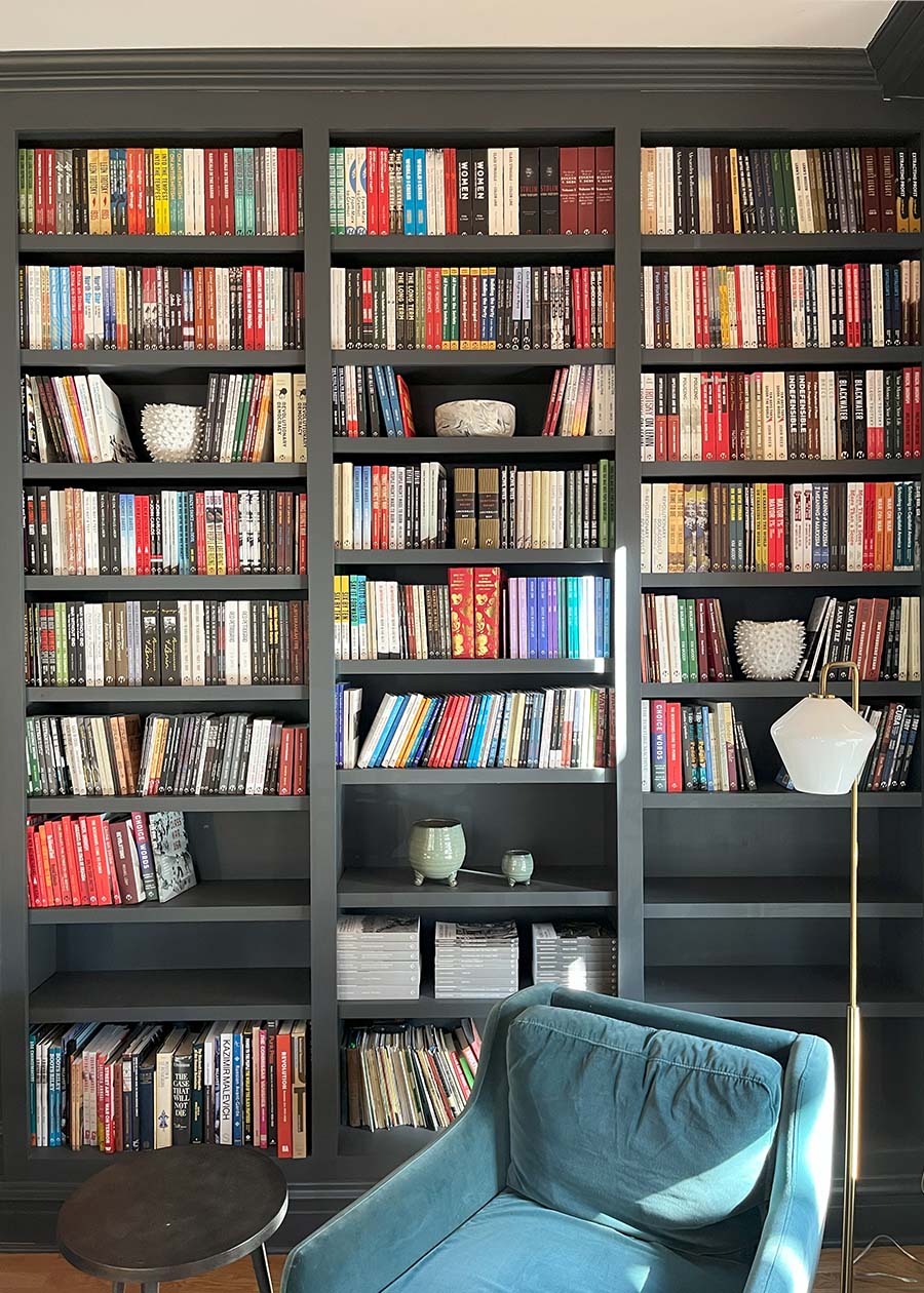 Library room at Haymarket House, with stacks of books covering multiple shelves and a turquoise chair in the foreground.